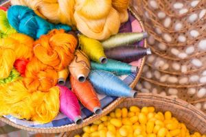 A vibrant assortment of colorful threads and yarns displayed in a woven basket, alongside a pile of yellow silk cocoons.